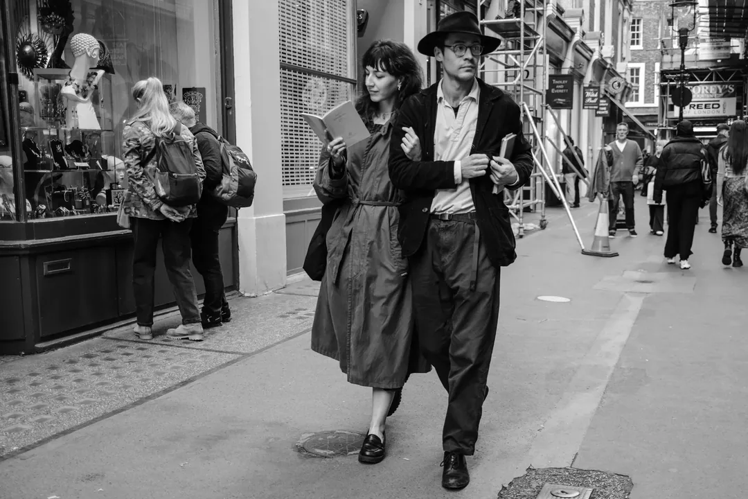 Een stel loopt arm in arm door een winkelstraat in Londen, zij leest in een boekje. Foto: Michiel Heijmans.
