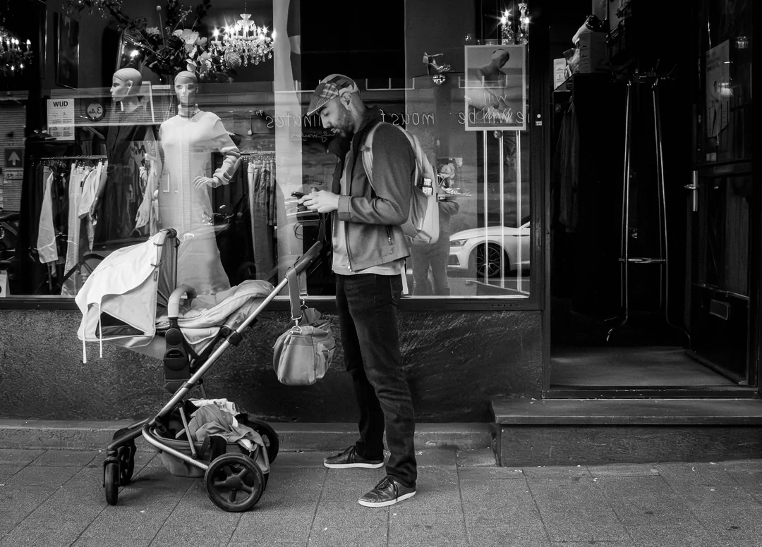 Een jonge vader met de kinderwagen die voor een dameskledingzaak staat te wachten